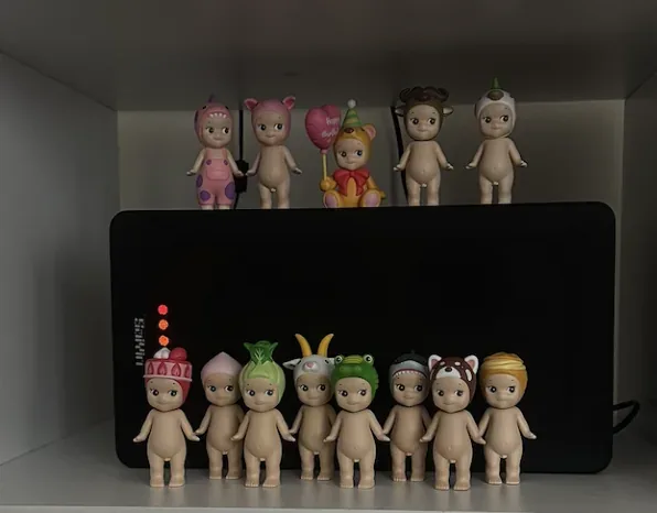 A Sonny Angel collection with varied animal and costume headpieces arranged in front of and above a black electronic device